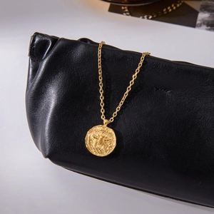 Detail of 18K gold stainless steel necklace featuring a bee coin pendant on a black bag