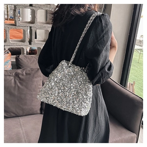 Close-up of sparkling silver sequin bucket bag with metal chain strap on model shoulder