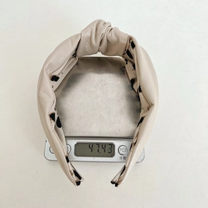 Beige knotted faux leather headband weighing 47.43g on a digital scale closeup