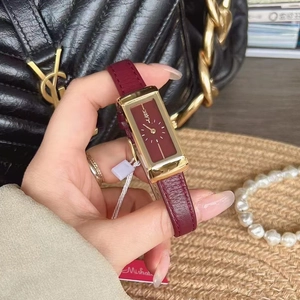 Close-up of rectangular gold watch with dark red dial and matching leather strap
