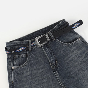 Detail of vintage silver buckle on a black ethnic embroidered belt with denim jeans