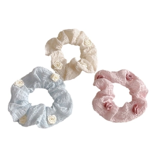 Three camellia fabric hair scrunchies in beige, light blue, and pink on white background