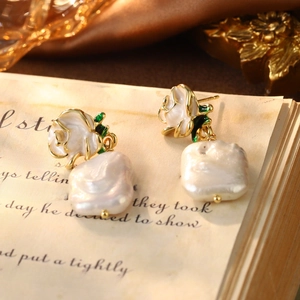 Close-up of vintage enamel white rose earrings with baroque pearls on silk background