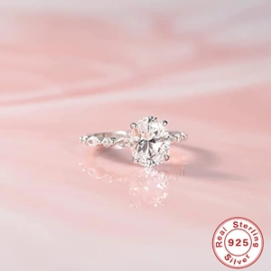 Detailed close-up of a silver ring with an oval diamond on a glossy pink surface