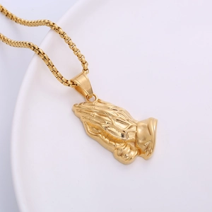 Polished 18k gold plated stainless steel praying hands pendant necklace on white ceramic plate
