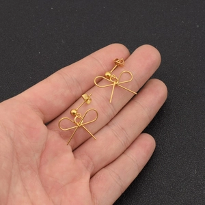 Detail of matte gold bow earrings held by hand over a dark textured surface