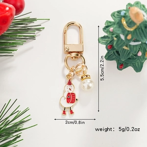 Christmas snowman keychain with gold ring and pearl charm against pine branches