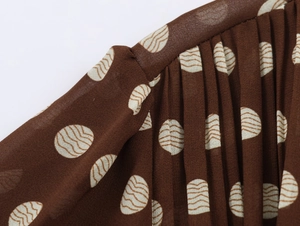 Close-up of pleated brown polka dot fabric showing detailed texture and pleat design