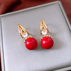 Macro detail of gold zircon earrings with red resin charms on a silk surface