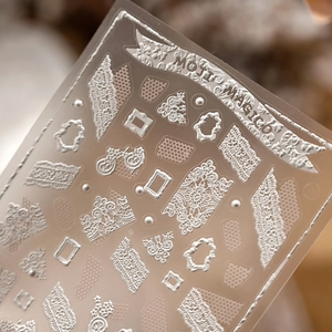 Macro shot of silver 3D embossed nail stickers with vintage lace and frame patterns