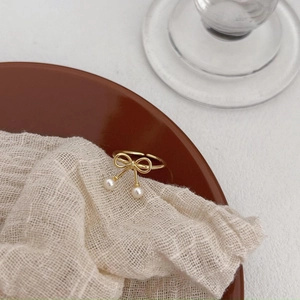 Detail of adjustable gold bow ring with hanging pearls on a ceramic dish