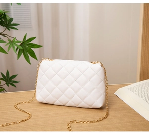 Detail view of white quilted crossbody bag with gold chain strap on a wooden desk