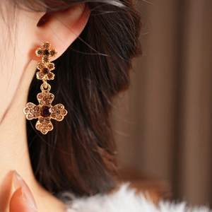 Detailed close-up of a vintage gold cross earring with amber crystal studs on a model