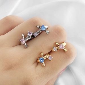 Detail showing heart-shaped Cupid arrow earrings on a fingertip for size reference