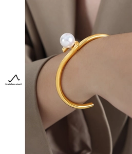 Detail of a gold open cuff bracelet with a large pearl worn over a beige sleeve