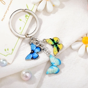 Macro detail of enamel butterfly keychain with three colorful charms on a white background