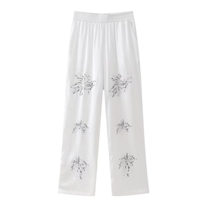 Detail of white satin wide-leg pants featuring black floral embroidery and elastic waist