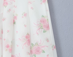 Close-up detail of white chiffon dress fabric featuring delicate pink rose floral patterns