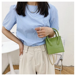 Close-up of green crocodile texture handbag with gold chain strap held by a model