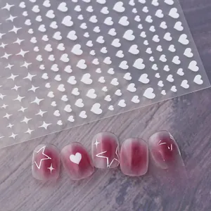 Detail of white heart and star nail art stickers on dark purple cat eye nail tips