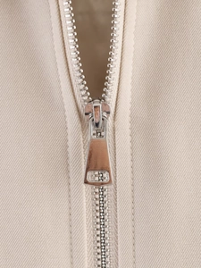 Macro shot of silver metal zipper on beige twill jacket highlighting fabric texture