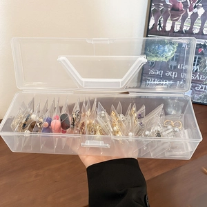 Detail of portable clear jewelry box with handle showing internal compartments for earrings