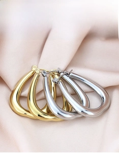 Close-up of gold and silver chunky teardrop hoop earrings on soft pink silk background
