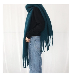 Dark green knitted scarf featuring soft fringe tassels worn by a model in soft light