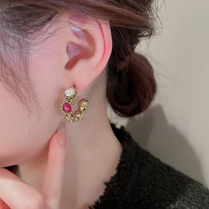 Detail of vintage golden C-shape earrings with texture and red zirconia on model