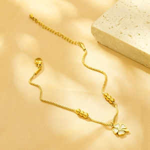 Detailed close-up of golden clover necklace with white shell inlay on beige fabric background