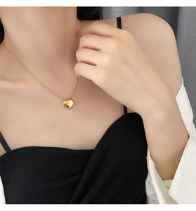 Detailed view of the gold heart pendant on a snake chain worn by a female model