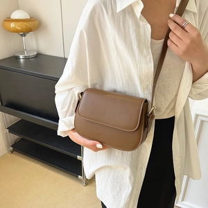 Minimalist brown leather crossbody bag with flap cover for women, shown on a shoulder