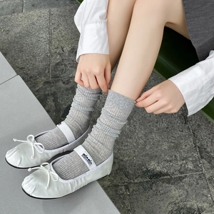 Detail of grey ribbed slouch socks styled with white ballet flats in a lifestyle setting