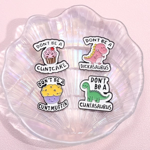 Cartoon enamel pins set featuring dinosaurs and cakes on a pearlescent shell tray