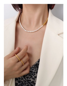 Detail of a gold-plated link chain pearl necklace and textured rings worn by a model