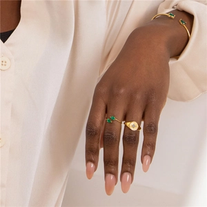 Detail of gold open bracelet and rings set featuring elegant green gemstone accents