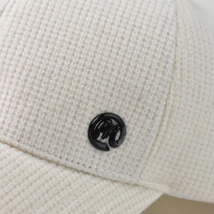 Macro shot of cream-white knitted baseball cap fabric with M-logo metal button detail