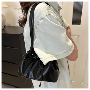 Detailed side view of a black drawstring bucket bag worn on the shoulder with leather straps