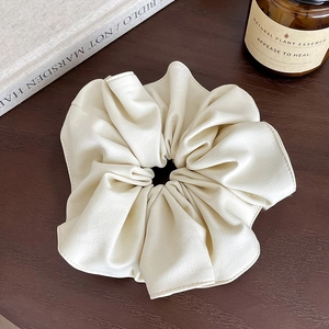 Détail du chouchou en cuir crème sur bureau en bois avec bougies et livres