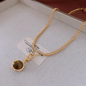 Detail of gold double-layered necklace featuring twisted chain and tiger eye pendant