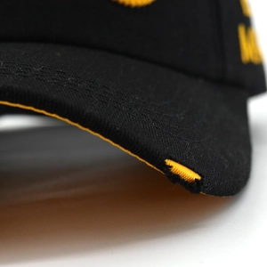 Detailed close-up of distressed brim on black cotton canvas baseball cap with yellow trim