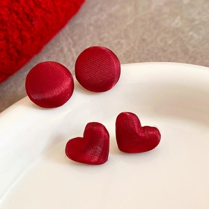 Dettaglio degli orecchini a lobo rossi a forma di cuore e tondi su un vassoio di ceramica bianca