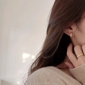 Close-up of gold-plated V-shaped earrings and textured ring on a female model