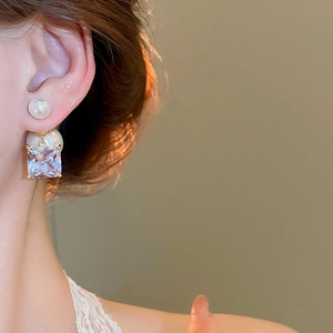 Detail shot of elegant double pearl earrings with a sparkling square zircon drop in gold