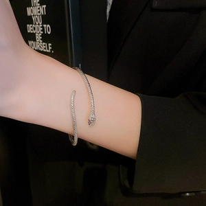 Detail van zilveren slangvormige open armband met rode edelsteenogen op een vrouwenpols