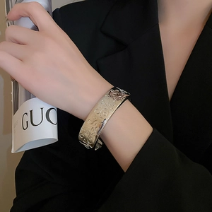 Close-up of a wide silver metal open cuff bracelet with vintage floral relief engraving