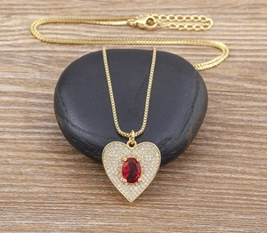 Detail of gold heart pendant necklace with red oval gemstone on dark stone background