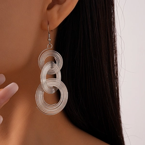 Close-up of hollow geometric silver coil tassel earrings worn by a model in detail