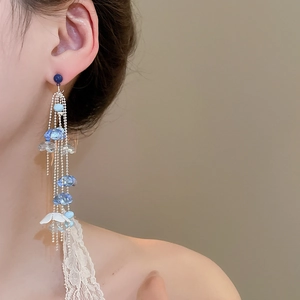 Detail of long blue beaded tassel earrings with white petal charm on model
