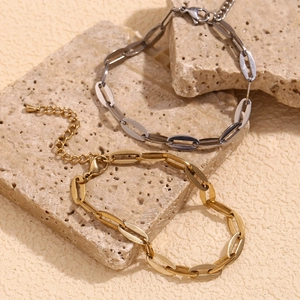 Detail view of gold and silver paperclip chain bracelets on a textured natural stone base